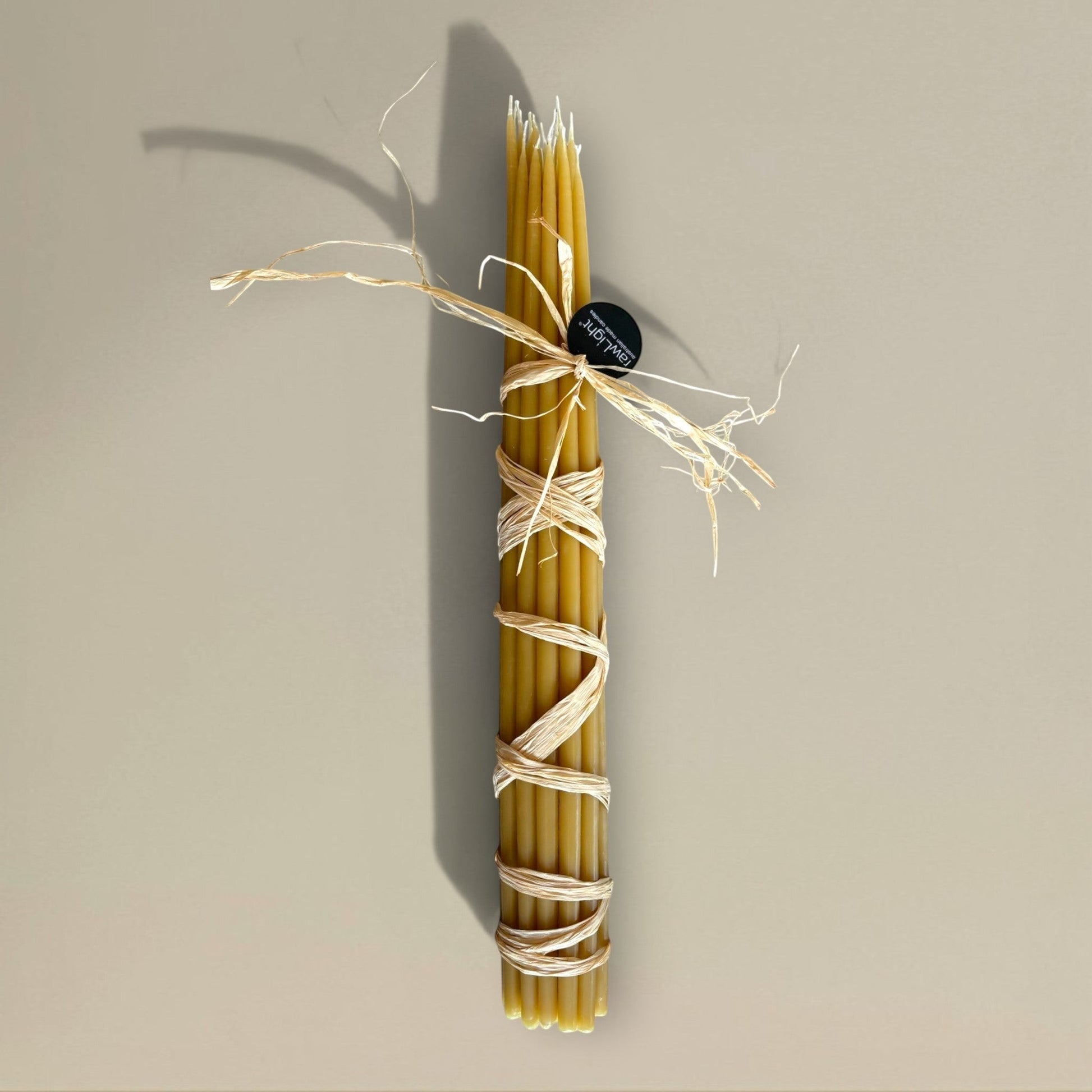Bundle of 22 rawLight beeswax prayer candles, 500mm tall, tied with raffia, natural golden amber colour.